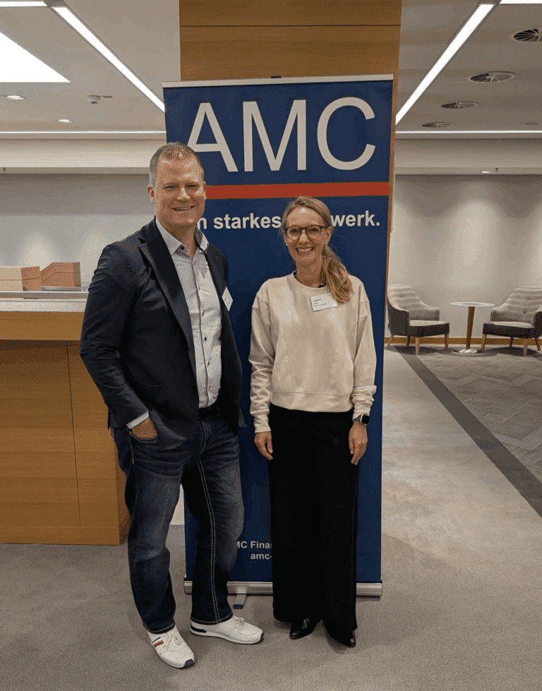 Marco Leven und Celine Spitz stehen vor dem AMC-Display auf der AMC Meeting 2025.