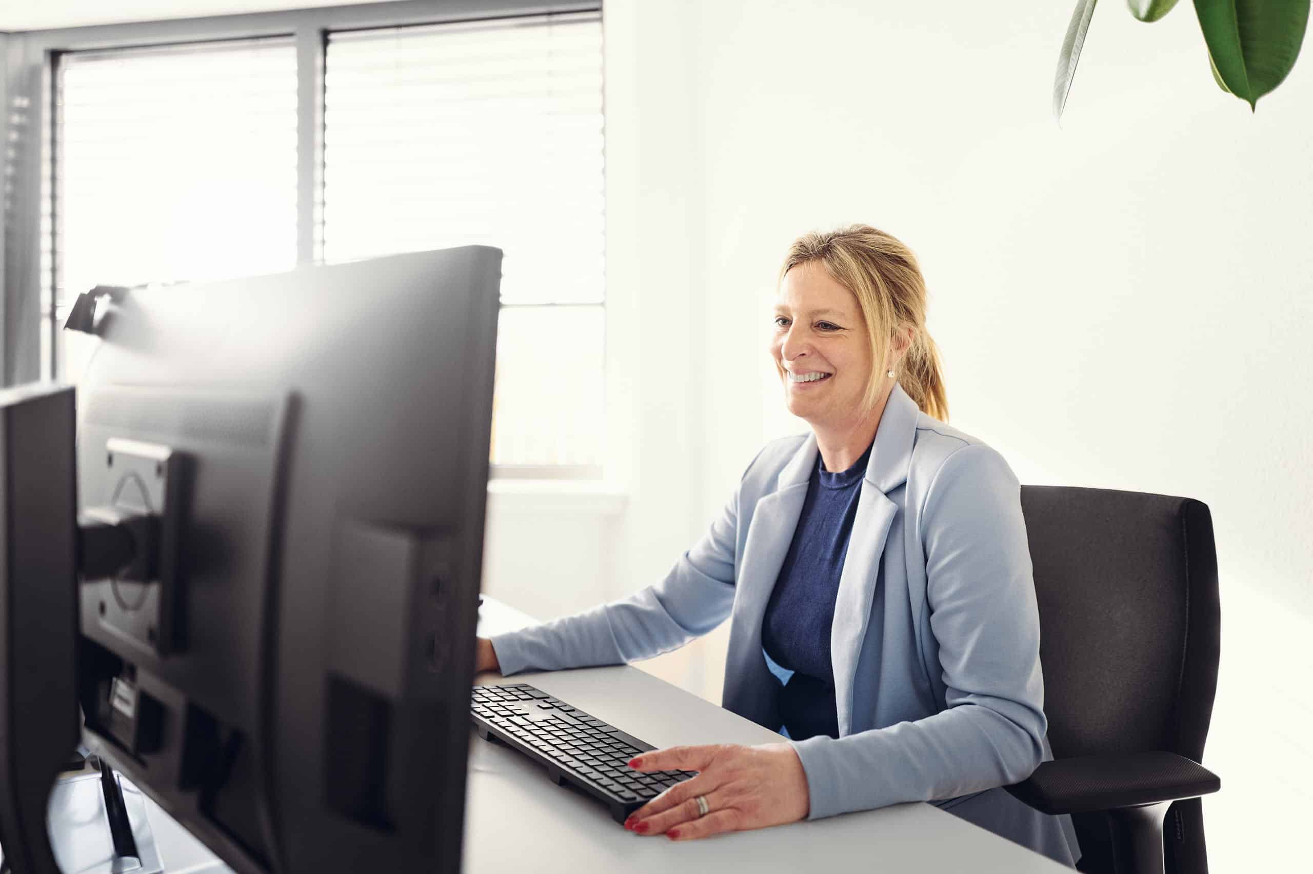 Christel Heusler sitzt lächelnd vor ihrem Computer und arbeitet.