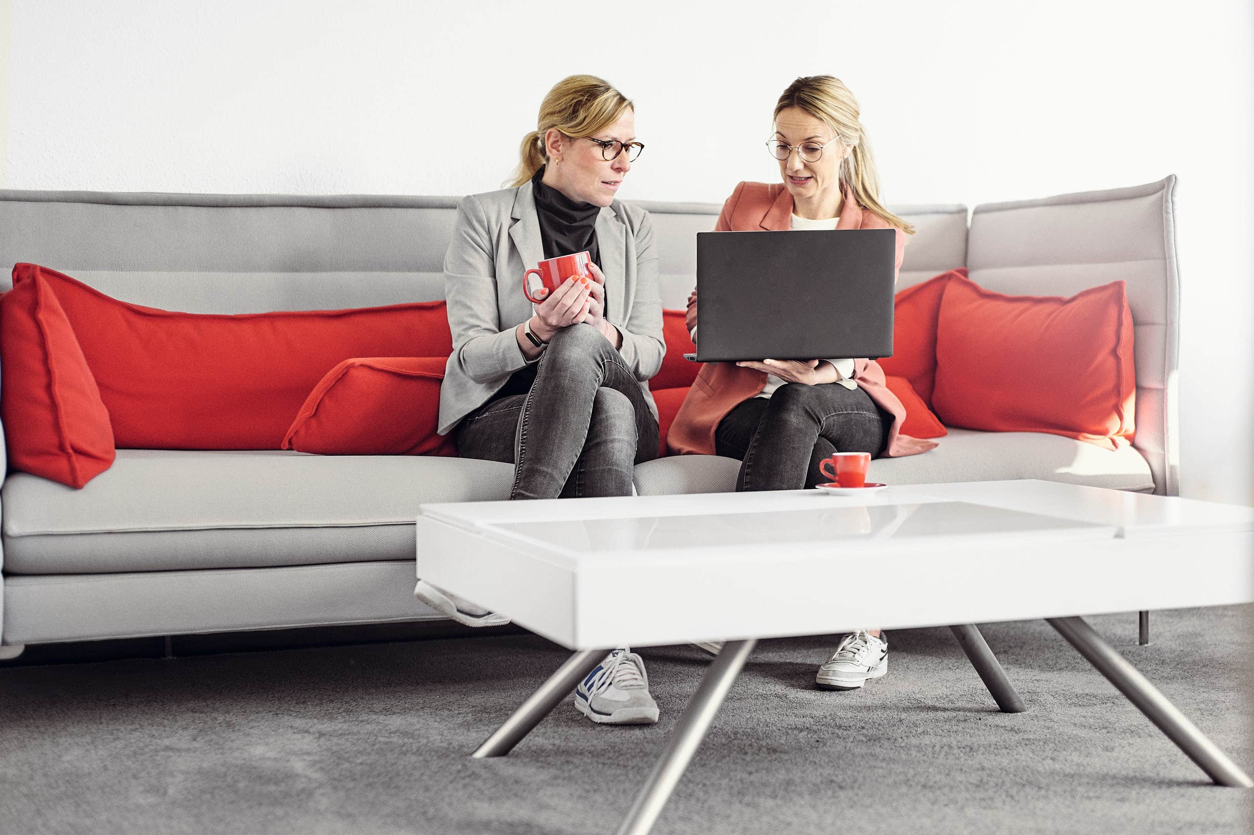 Celine Spitz und Magdalena Sabaß sitzen auf einem Sofa, während Celine Magdalena etwas auf ihrem Laptop erklärt.