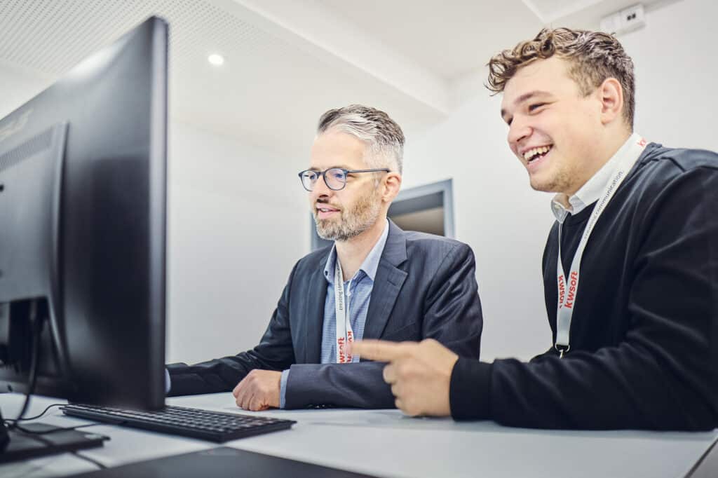 Julius Binninger und Markus Singer sitzen vor einem Bildschirm und schauen darauf.