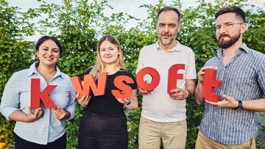 Zwei Frauen und zwei Männer halten rote Buchstaben, die das Wort kwsoft bilden.